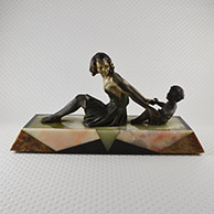 escultura en petit bronce fundido con pátina plateada y verde sobre base de mármol y ónice que representa una mujer joven que juega con un niño. Principio del siglo XX